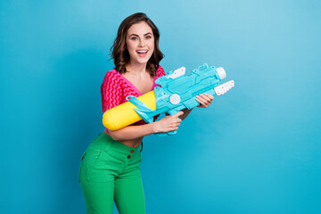 Photo of optimistic good mood gorgeous girl with curly hairdo dressed pink top holding water gun isolated on blue color background