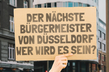 The phrase " Who's the next mayor of D&uuml;sseldorf? " on a banner in men's hands blurred the background. Election. City management. Politics. Urban. Voter. Candidate