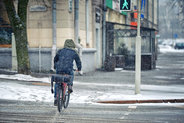 Delivery man on bicycle cycling with pizza bag on snowy street in winter season. Food delivery...