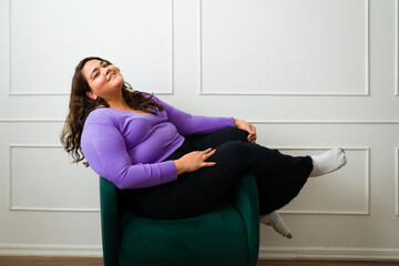 Cheerful big woman relaxing on a chair and smiling - obrazy, fototapety, plakaty