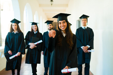 Attractive woman pointing wearing a graduation gown