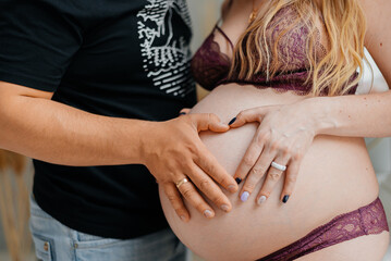 Pregnant woman and her husband holding hand in heart shape on baby bump. Close up of couple making heart shape on the tummy. Loving future couple expecting a baby