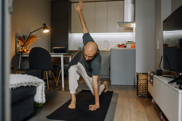 A young man in home clothes is doing sports stretching in the living room in a modern apartment