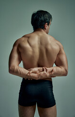 Rear view of strong muscular relief male's back. Handsome young model posing in black underwear over studio background. Concept of man's beauty, sportive and healthy lifestyle, fashion