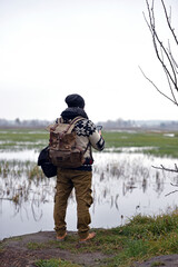 A young guy with a backpack. traveller, hipster standing on the shore of a pond. flooded meadows. looking into the distance, Hiking, Forest, Journey. man, back view. beauty of nature