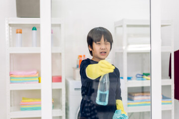 Kid little asian boy son having fun doing household cleaning and washing in protective gloves using...