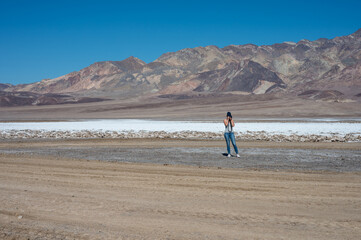 Fototapeta na wymiar a young girl in the distance taking photos of the desert landscapein Badwater Basin desert in Death Valley