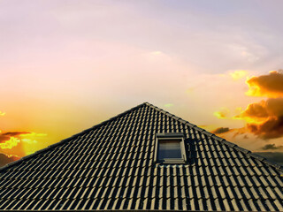 Colorful sunset. Open roof window in velux style with black roof tiles.