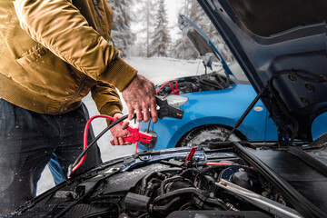 Automobile starter battery problem in winter cold weather conditions. mechanic using jumper cables to start-up a car engine. Low battery.
