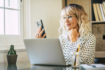 Cheerful happy businesswoman doing phone call in front of a laptop computer in home office...