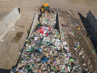 Skid steer loader moving plastic garbage with scrap grapple on the landfill site, drone shot. Waste...