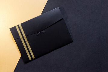 black envelope mockup, Flat Lay, on black and gold background with copy space. Tied with a gold ribbon.