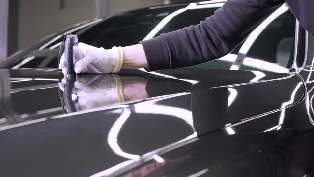 Worker measures a thickness of primer on a car's body using a thickness gauge