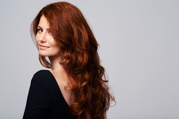Terrific tresses. Studio shot of a young woman with beautiful red hair posing against a gray...