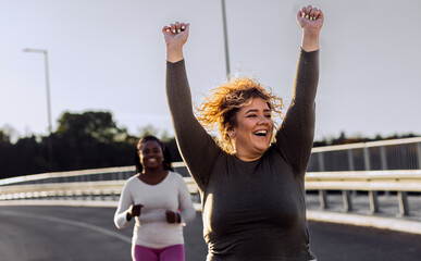 Two excited young plus size women jogging together. - obrazy, fototapety, plakaty