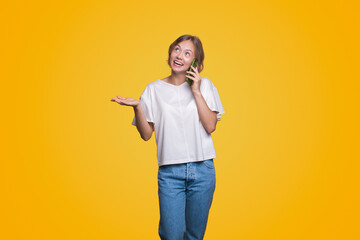 Smiling happy woman talking on mobile cell phone conducting pleasant conversation and looking away over yellow background.