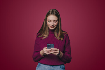 Brunette smiling young woman using cell phone, messaging, being happy to text with her friends isolated over pink background. Modern technologies and