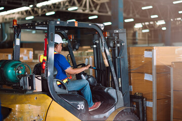 Asian male warehouse worker driving forklift for loading pallets in warehouse to container.