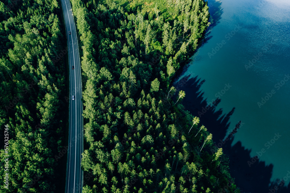 Wall mural Aerial view road through green woods and blue lake in Finland.