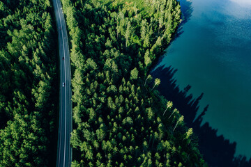 Aerial view road through green woods and blue lake in Finland.
