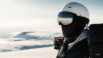 A skier in a helmet and glasses in winter gear is going to conquer the top of the mountain on a snowboard.