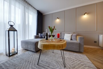 Przytulny apartament z wygidą sofą, na pierwszysm planie stolik kawowy z butelką wina i kieliszkami