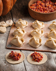 Semi-finished manti oriental dumplings on wooden board with flour