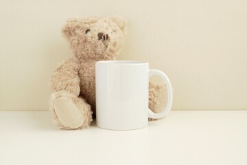 White mug mockup with teddy bear soft toy for kids design presentation.