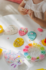 Fototapeta na wymiar Child hands creating Easter eggs from play dough decoration with beads. Cute children's crafts for Easter. Holiday Art Activity for Kids. Fine motor skills, creativity and hobby.