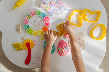 Child hands creating Easter eggs from play dough decoration with beads. Cute children's crafts for Easter. Holiday Art Activity for Kids. Fine motor skills, creativity and  hobby.