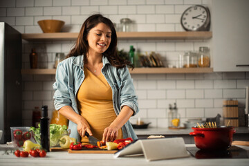 Young woman cutting vegetables in kitchen. Beautiful pregnant woman making salad.