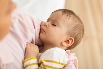 Closeup portrait of adorable sleeping baby girl in mother's arms, caring mother lulling daughter