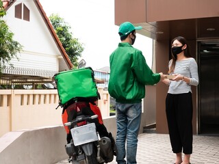 Asian delivery man ride motorcycle and wear green uniform pick up food and deliver to customer at...
