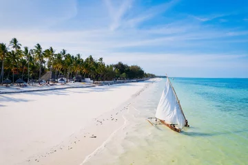 Fototapeten Relax on the white sand beach in Kiwengwa village on Zanzibar while admiring a Dhow catamaran sailboat gently gliding through the crystal-clear waters. © Sebastian