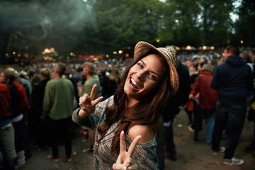  Its all about the vibe. A pretty young woman showing a peace sign at an outdoor music festival. © Jeff B/peopleimages.com
