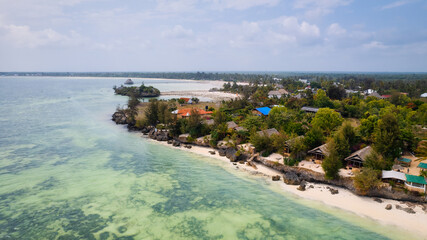 The aerial view of Zanzibar's Indian Ocean coastline is simply stunning, featuring palm trees, white sand, and sparkling blue waters. With luxurious hotels and a tropical landscape, it is the perfect 