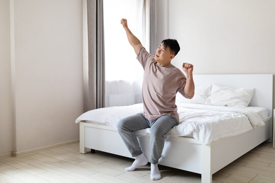 Smiling asian man enjoying happy morning, stretching in bed