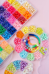 Kids handmade beaded jewelry and different multi-colored beads for children's needlework and crafts in boxes. DIY art activity for kids. Motor skills, creativity and  hobby.