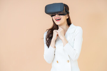 portrait of a young asia woman wearing a white cardigan and VR glasses. She is amazed by what she is seeing. Virtual reality headset. isolated orange background
