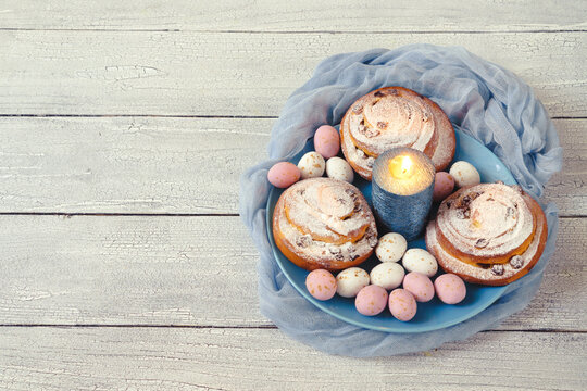 Easter decor with sugar flowers and chocolate eggs with round spiral buns on a blue plate