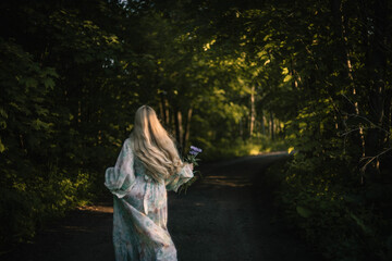 blonde woman with long hair in a dress walks through the forest, the concept of the beginning of summer.