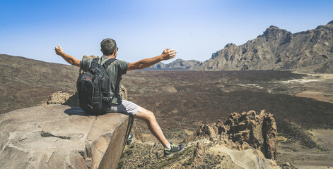 Man open arms enjoying a beautiful panorama Boy sitting on a mountain cliff. Freedom outdoor concept