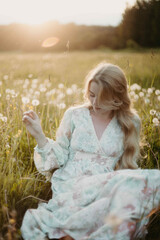 young woman in a dress in a dandelion field at sunset, the concept of the onset of summer, vacation dreams and memories.