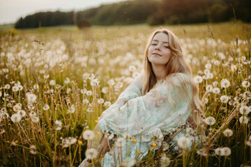 young woman in a dress in a dandelion field at sunset, the concept of the onset of summer, vacation dreams and memories.