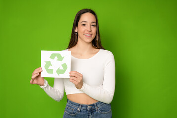 Positive smiling woman holding green symbol, sorting rubbish, saving environment, wearing white T-shirt. Indoor studio shot isolated on green background.