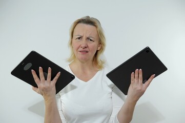 woman has two tablets in hands she is unhappy looks into frame tired of work an overabundance of information burnt out at work white background white clothes Studio no dyed hair no time for yourself - obrazy, fototapety, plakaty