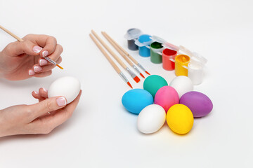 Holidays, tradition and people concept - close up of woman hands coloring easter eggs with brush