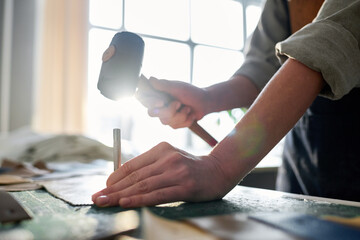 Close-up of hands of young tanner going to hit top of small steel shaft with hammer while working in craft shop in the morning