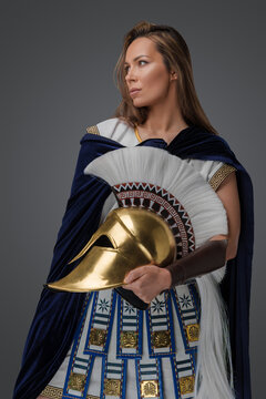Studio shot of greek warlord woman dressed in armor holding golden helmet.