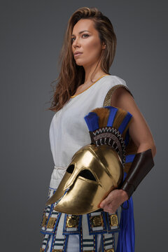 Portrait of ancient female soldier with golden helmet against gray background.